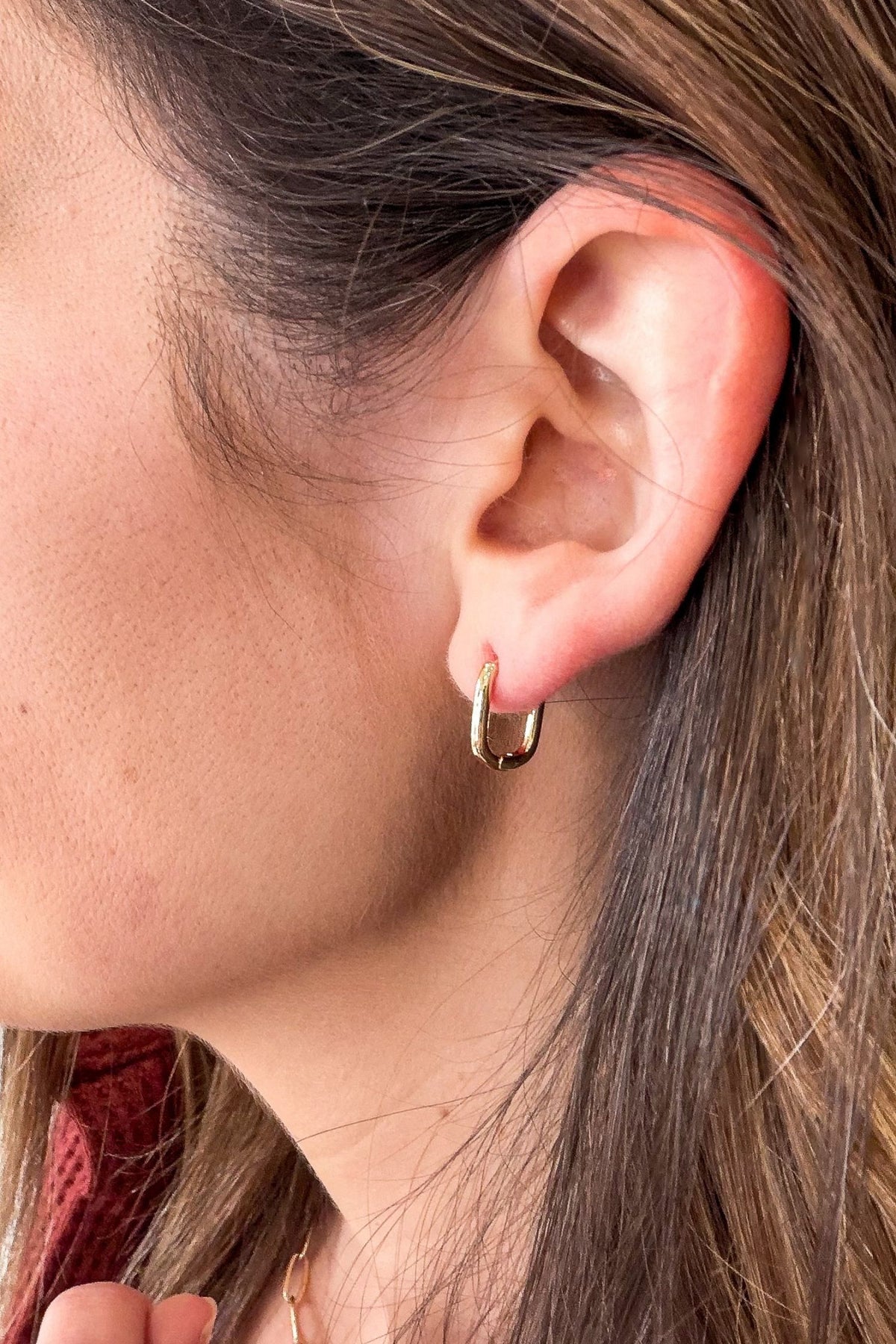 A close-up side profile of a person's ear wearing a small gold hoop earring.