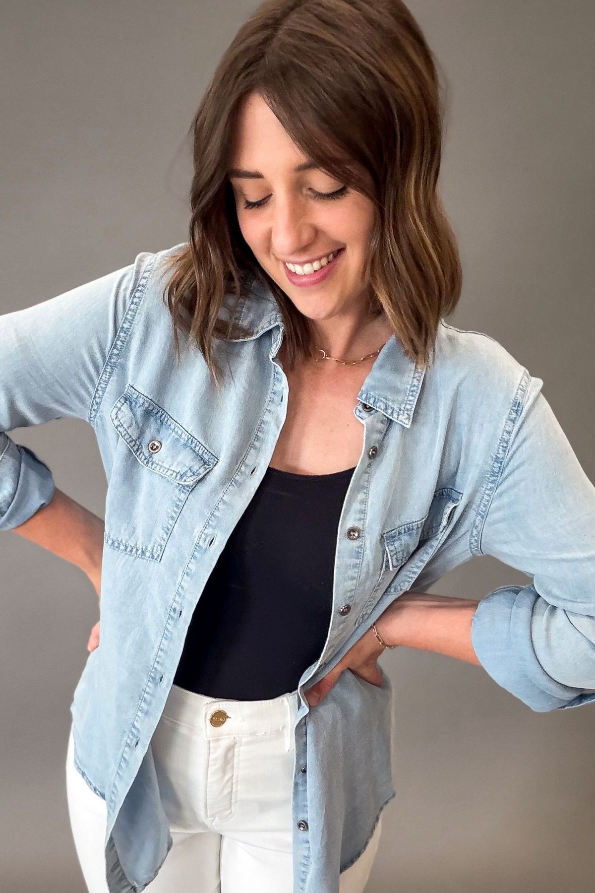 Woman wearing a light blue chambray buttonup over a black top on a gray background
