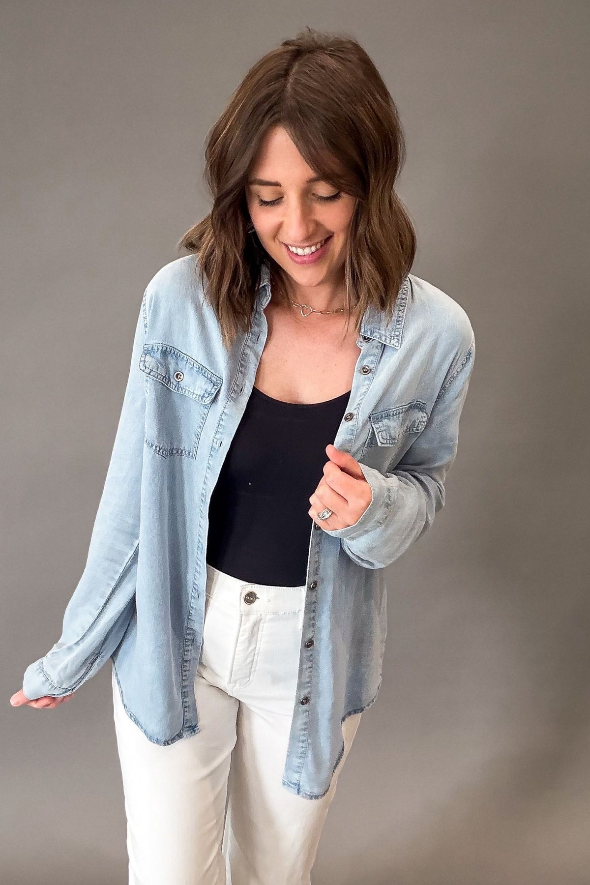 Woman wearing a light blue chambray buttonup over a black top on a gray background