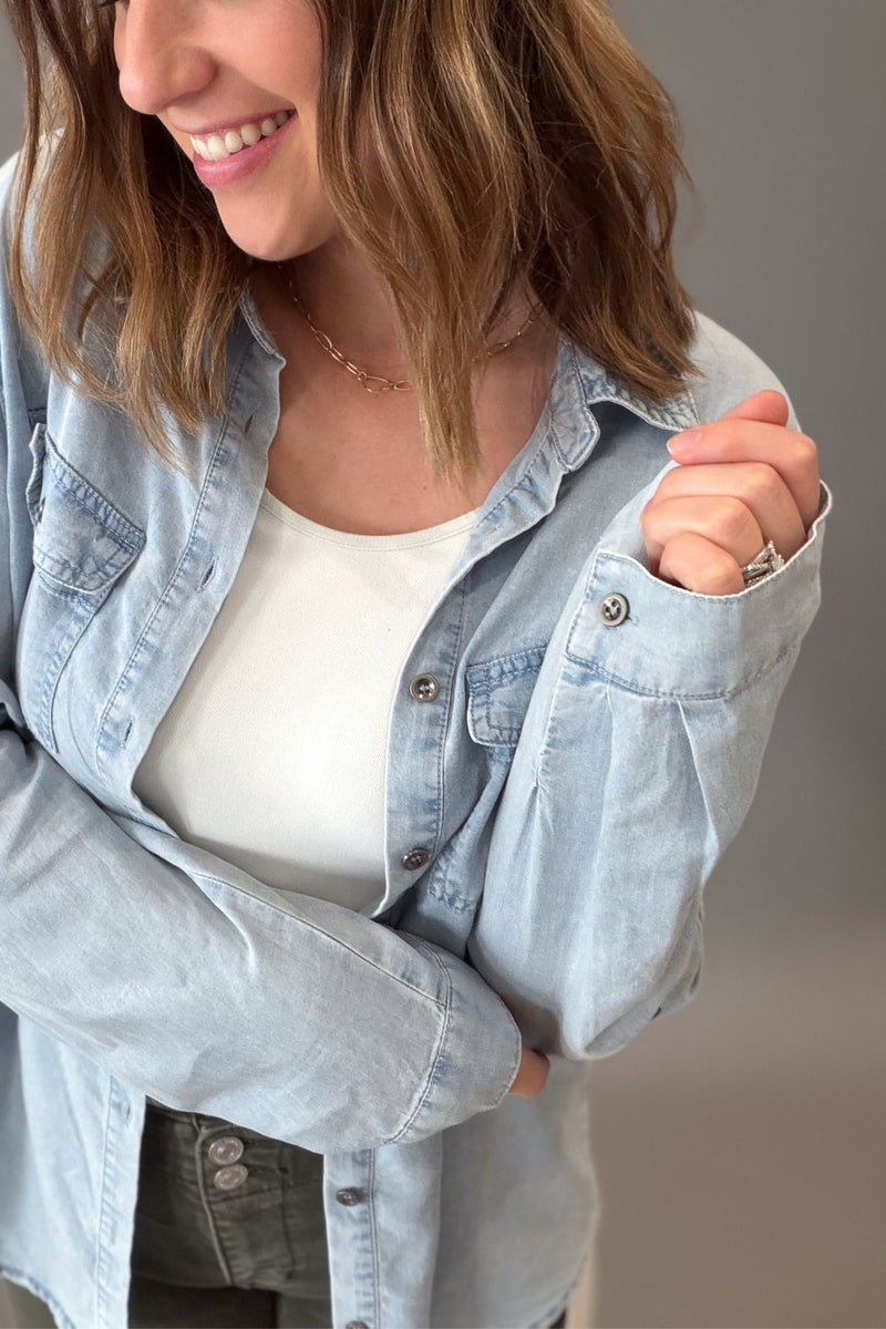 a woman that has shoulder length hair wearing a chambray button front button up with a white tank and olive mica denim showing the closeup details.