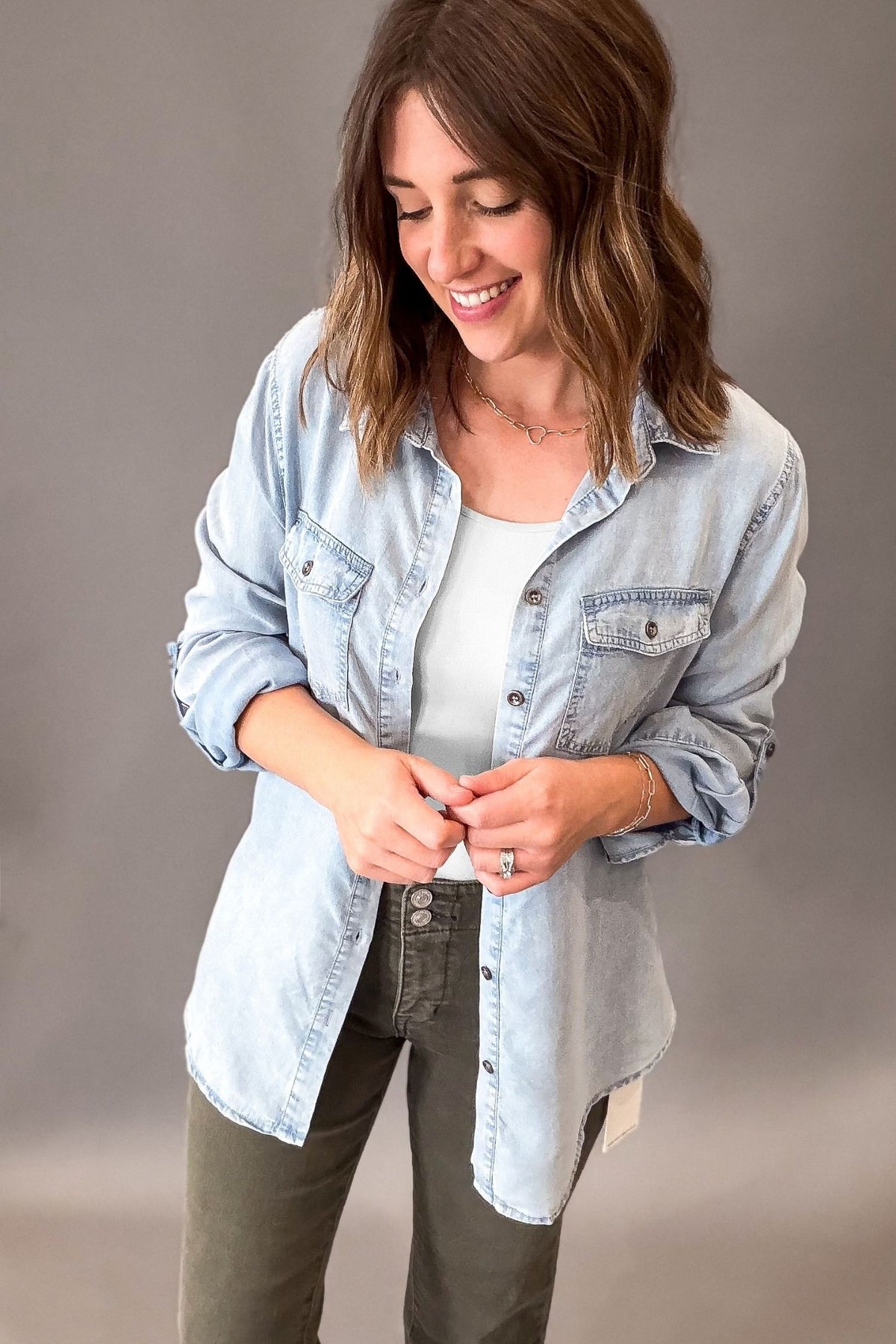 a woman that has shoulder length hair wearing a chambray button front button up with a white tank and olive mica denim