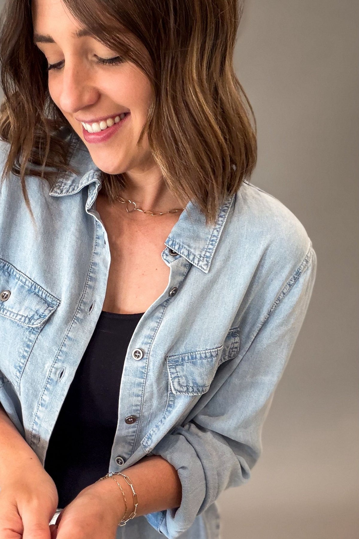 Woman wearing a light blue chambray button up against a neutral background