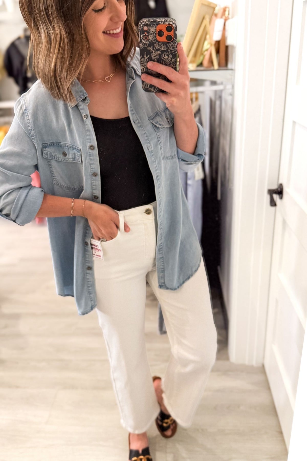 Woman taking a mirror selfie wearing a tencel button up, black top, and white pants.