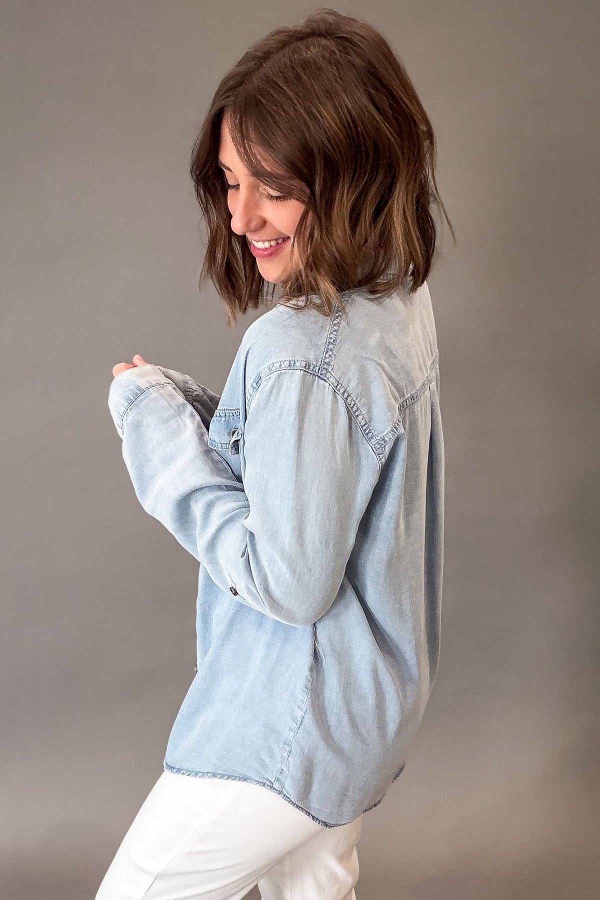 Woman wearing a light blue chambray button up against a plain background