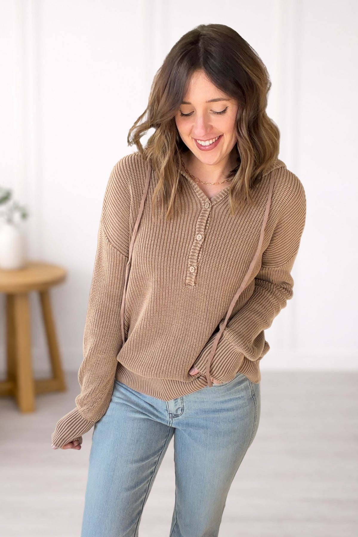 Woman wearing a brown sweater and light blue jeans indoors.