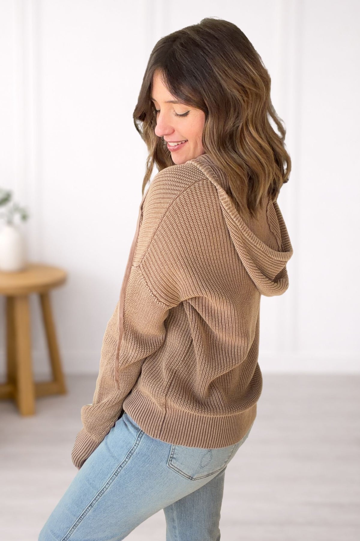 Woman wearing a brown sweater and light blue jeans in a minimalistic setting