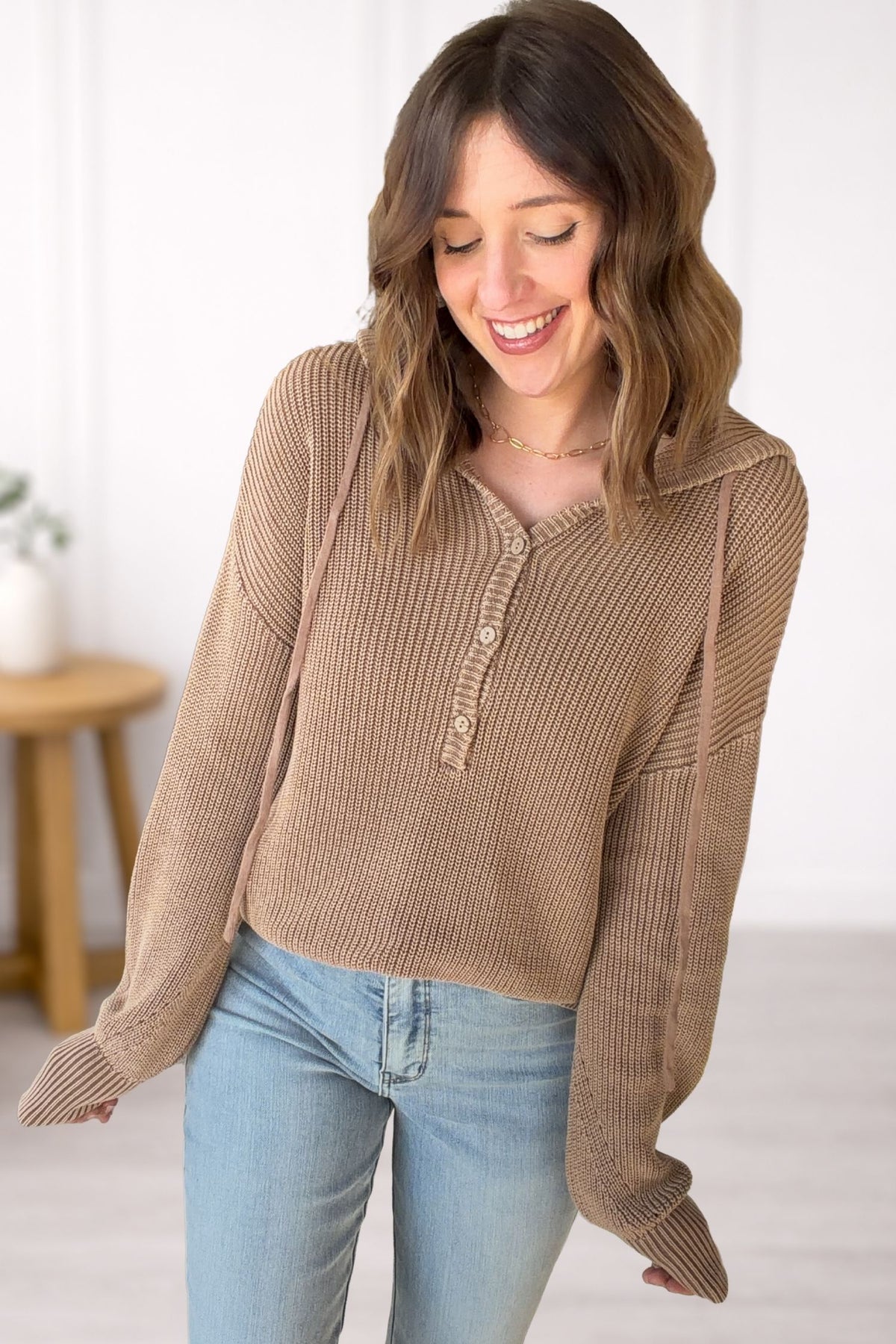 Woman wearing a brown ribbed sweater and blue jeans against a white background