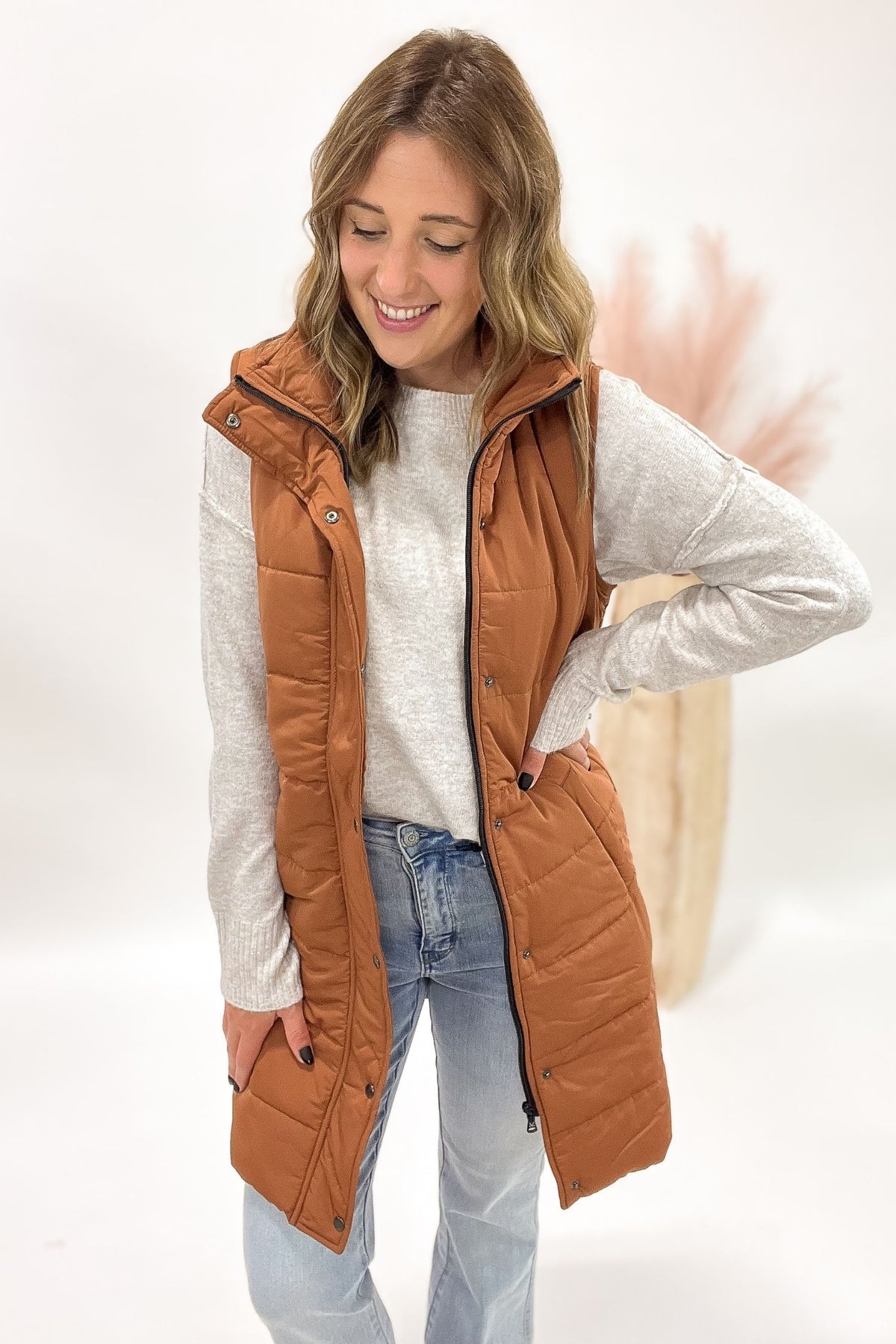 Woman wearing a copper puffer vest over a white shirt and blue jeans on a white background