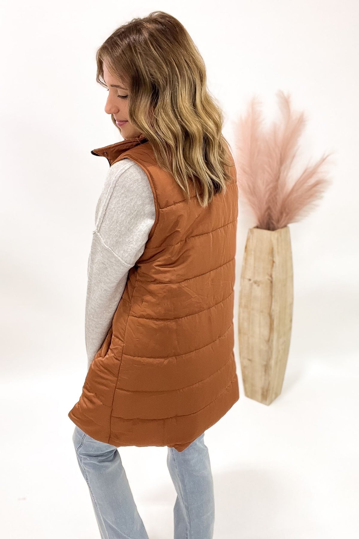 Woman wearing a copper puffer vest with a white background