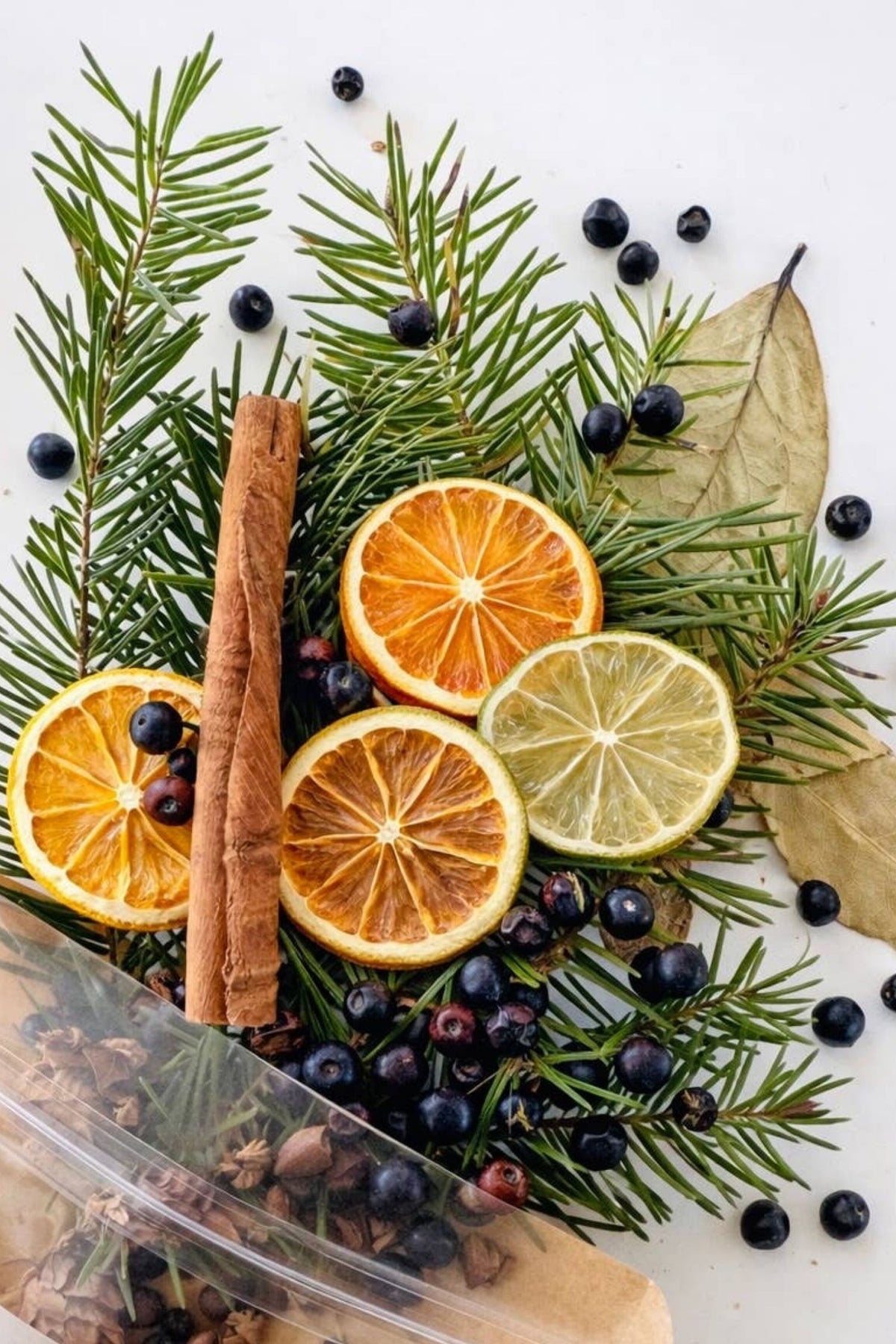 Decorative arrangement of citrus slices, cinnamon sticks, pine, and berries on a white background
