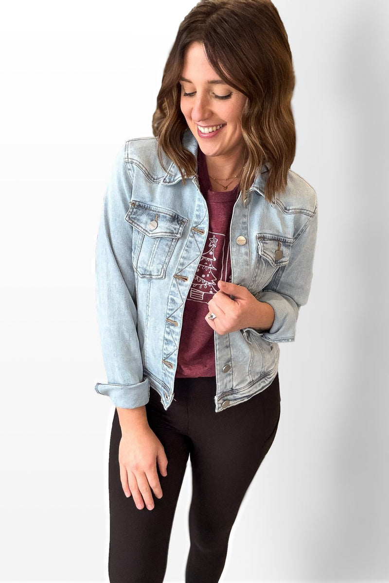 Woman wearing a light blue denim jacket over a maroon shirt and black pants on a white background