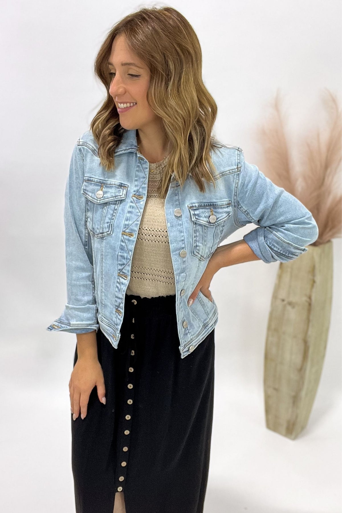 Woman wearing a light blue denim jacket over a beige top and black skirt on a white background