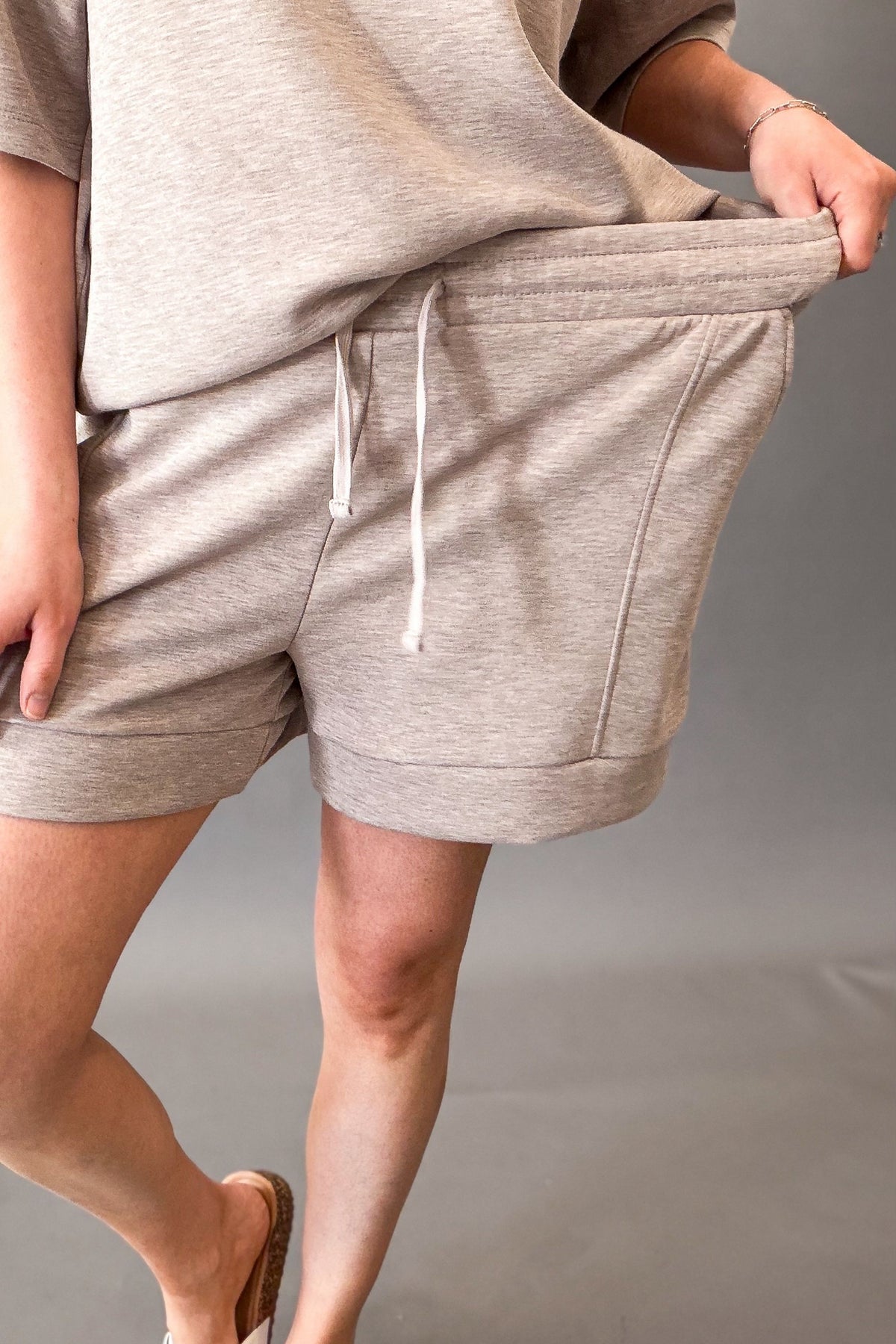 woman wearing a drawstring heather taupe short showing lots of stretch in the waistband