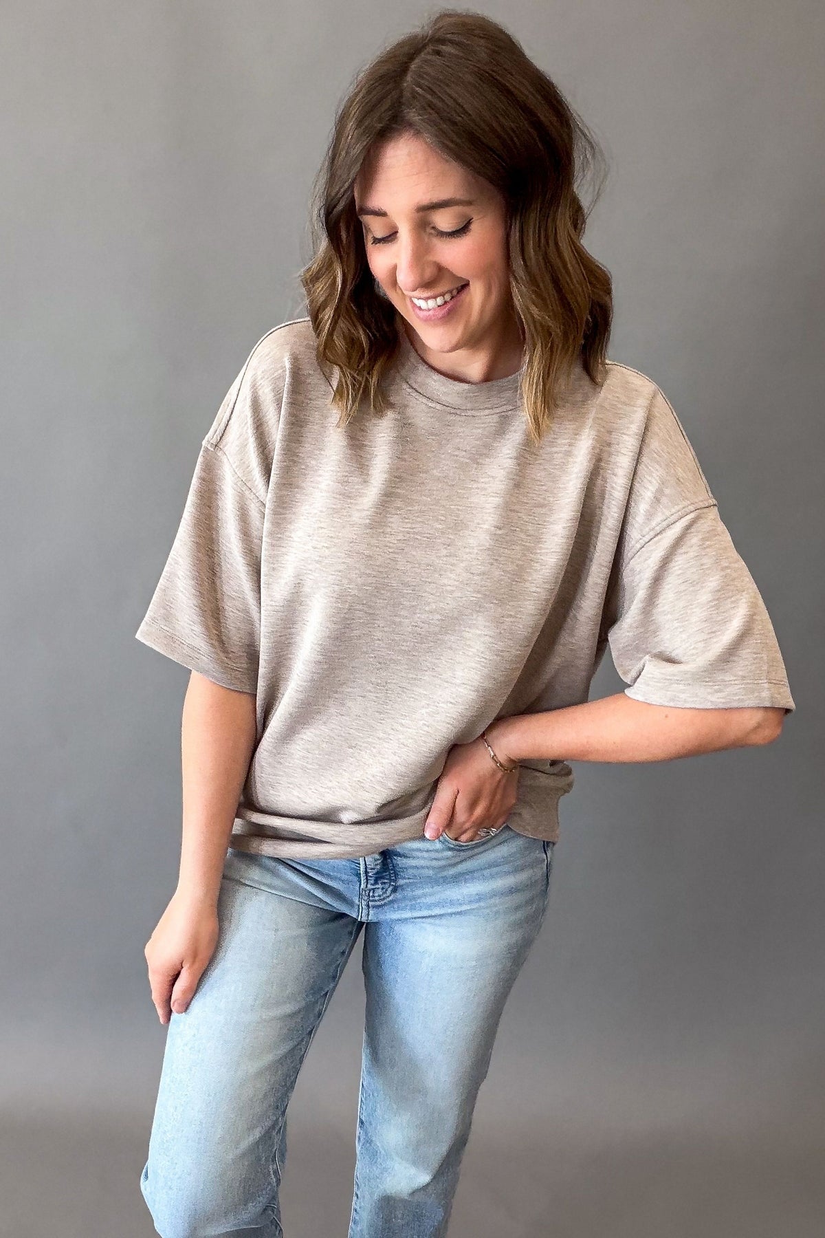 woman wearing a relaxed short sleeve top with blue jeans on a grey background