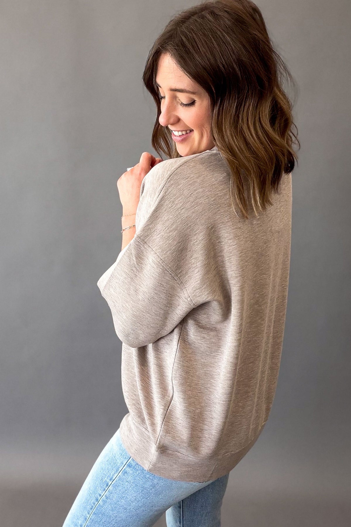 woman wearing a heather taupe short sleeve showing the longer sleeve length and back details