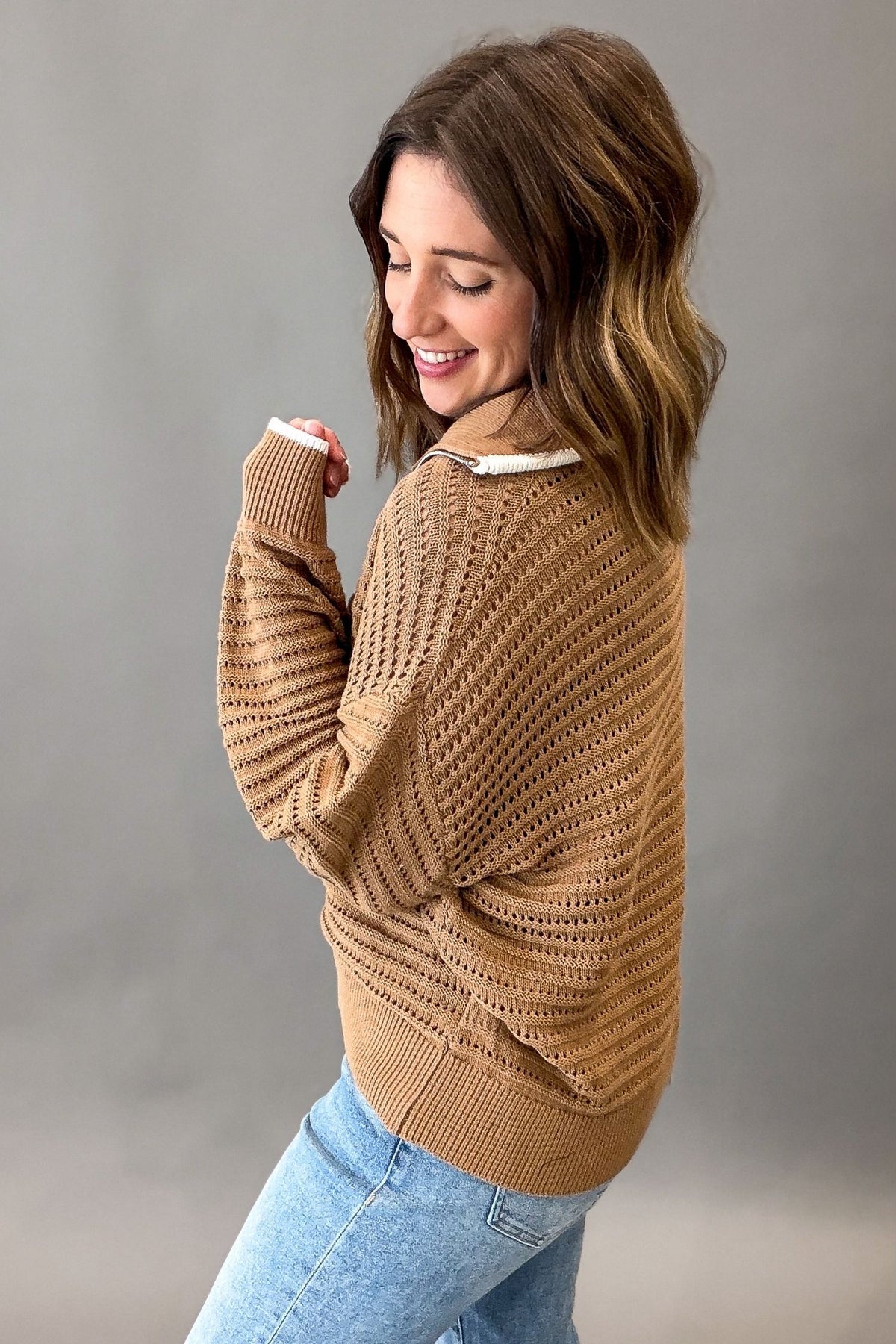 A woman wearing a coconut-colored textured knit sweater and light blue jeans, photographed against a neutral gray studio background.
