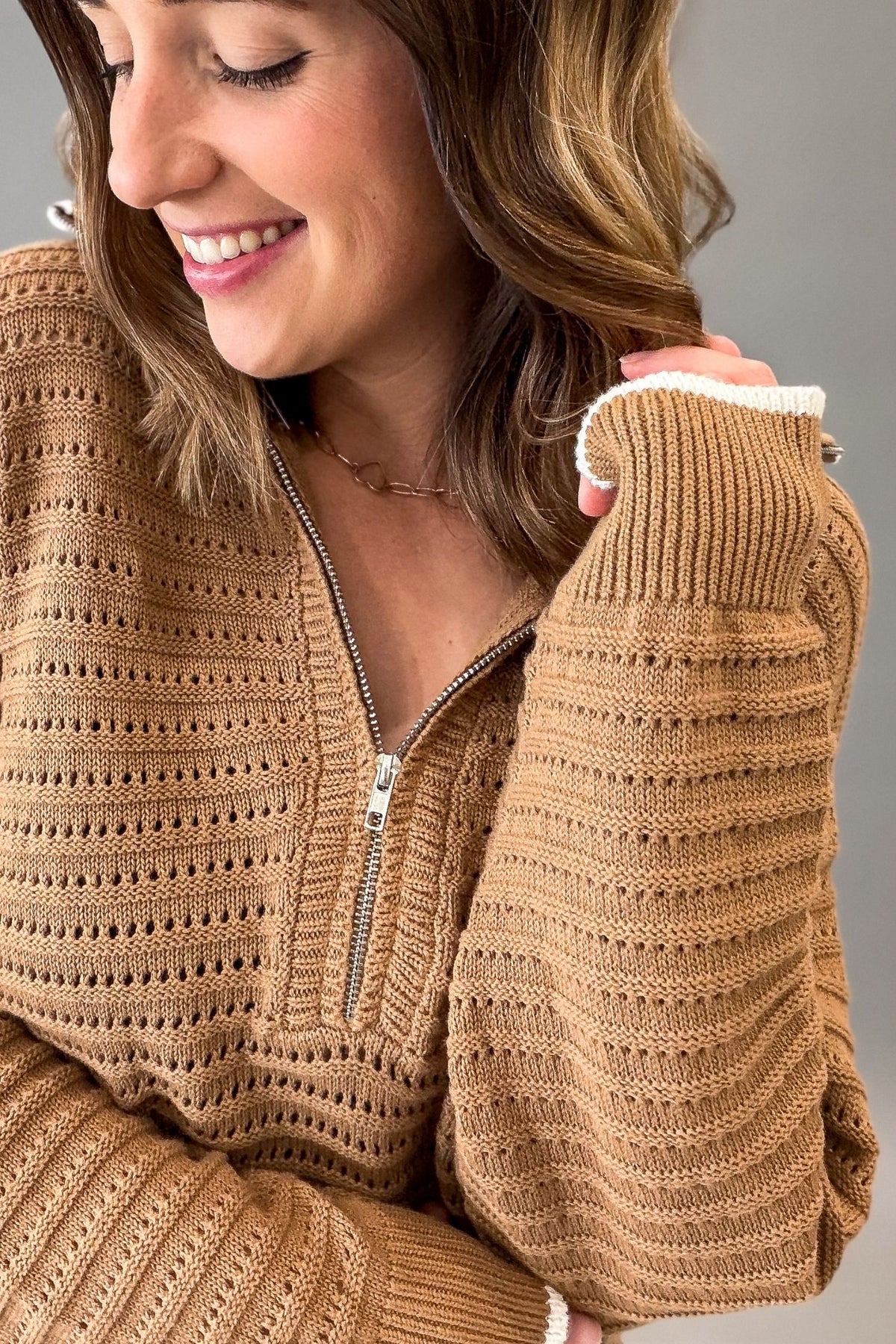 A close-up of a woman wearing a textured, ribbed knit half-zip sweater in a warm coconut brown color, with white ribbed trim at the cuffs.