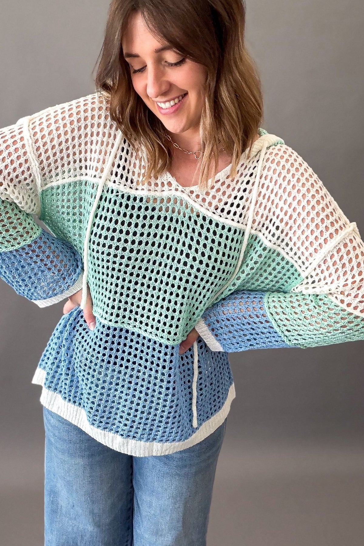 woman wearing a open knit coastal pullover and blue jeans on a grey background