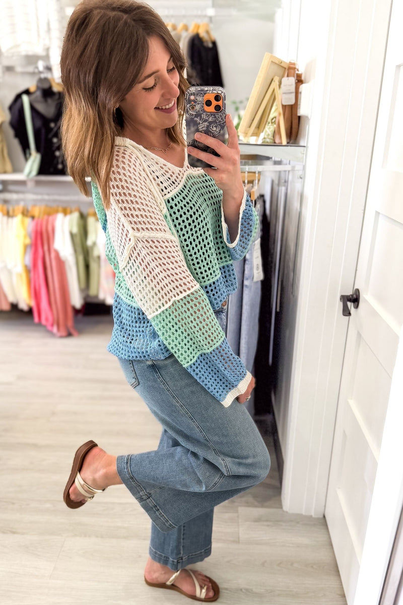 Woman wearing a blue mint ivory lightweight hoodie taking a mirror selfie in a boutique