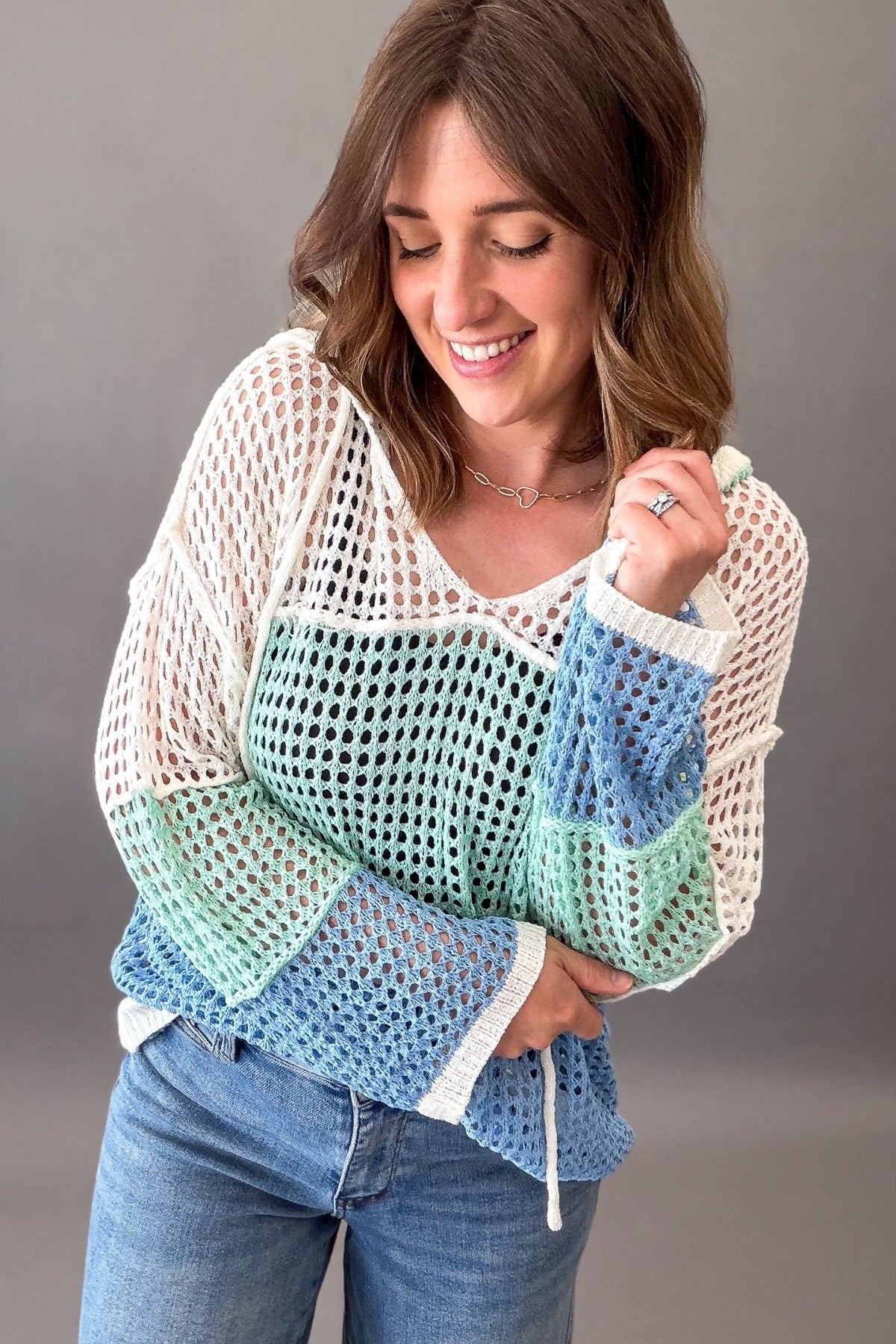 woman wearing a open weave color block hooded pullover with judy blue jeans on a charcoal background
