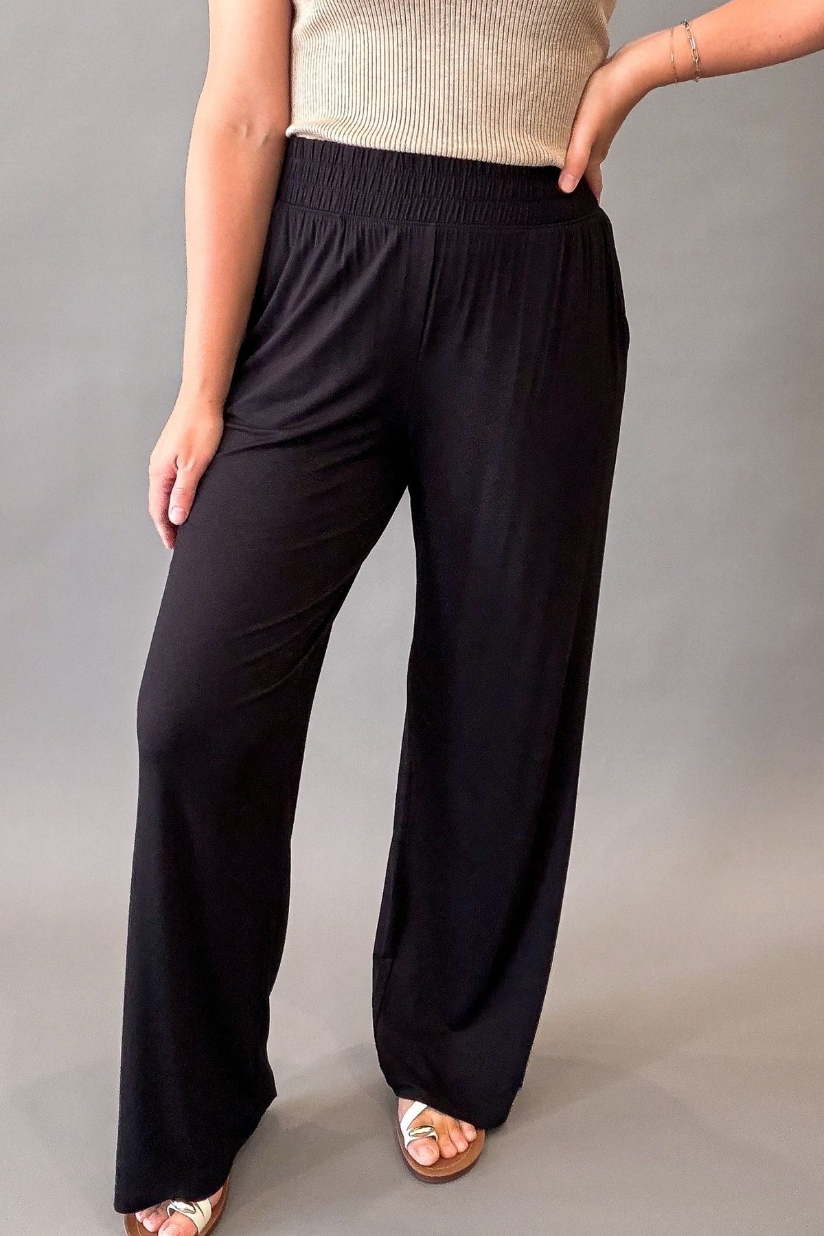 Woman wearing ultra-soft black wide leg pants with a stretchy elastic waistband and front pockets styled with sandals.