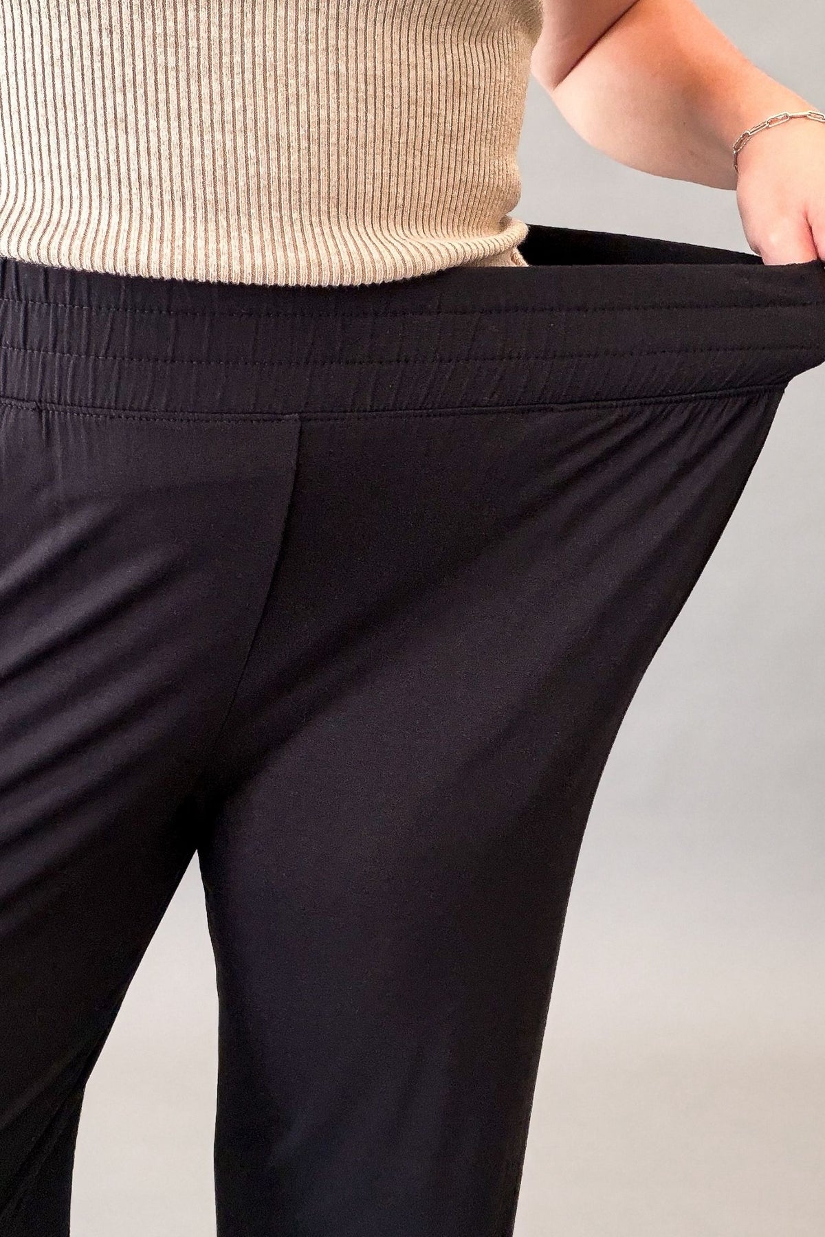 Woman wearing ultra-soft black wide leg pants with a stretchy elastic waistband and front pockets styled with sandals.