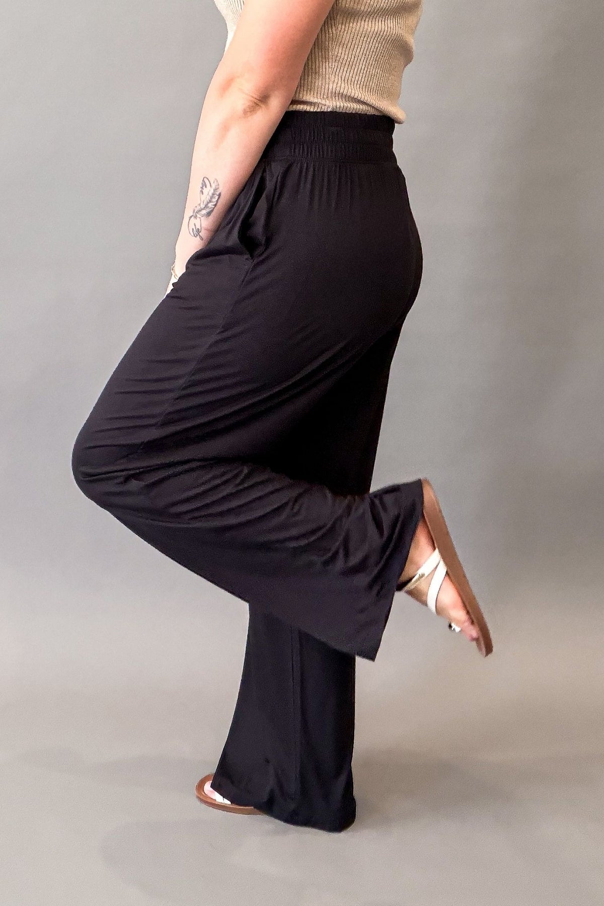 Woman wearing ultra-soft black wide leg pants with a stretchy elastic waistband and front pockets styled with sandals showing the side details of the pants
