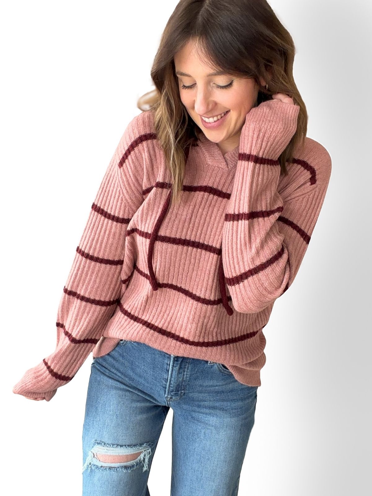 Woman wearing a pink sweater with red stripes and blue jeans on a white background