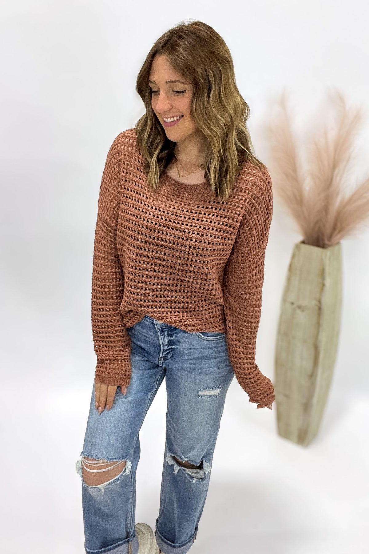 Woman wearing a copper crochet sweater and blue jeans against a white background