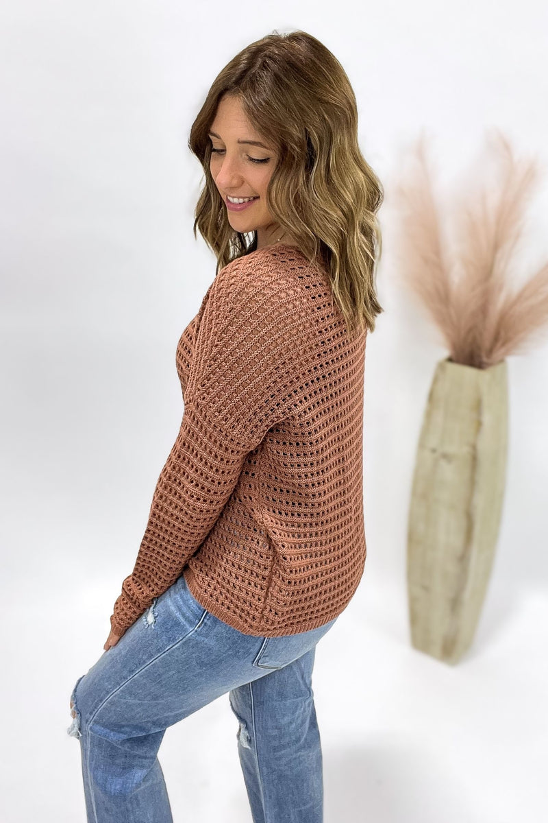 Woman wearing a copper crochet sweater and blue jeans against a white background