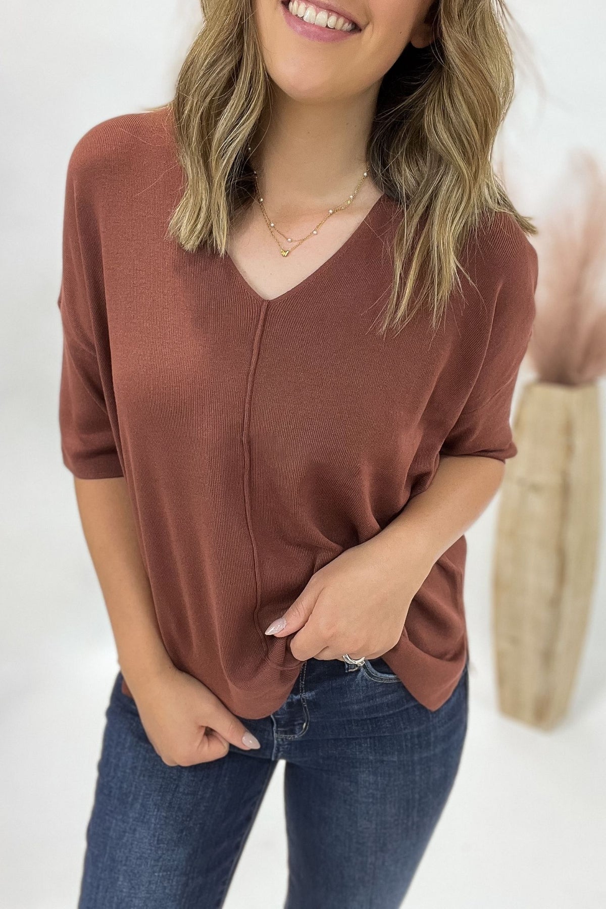 Woman wearing a copper sweater and blue jeans with a white background