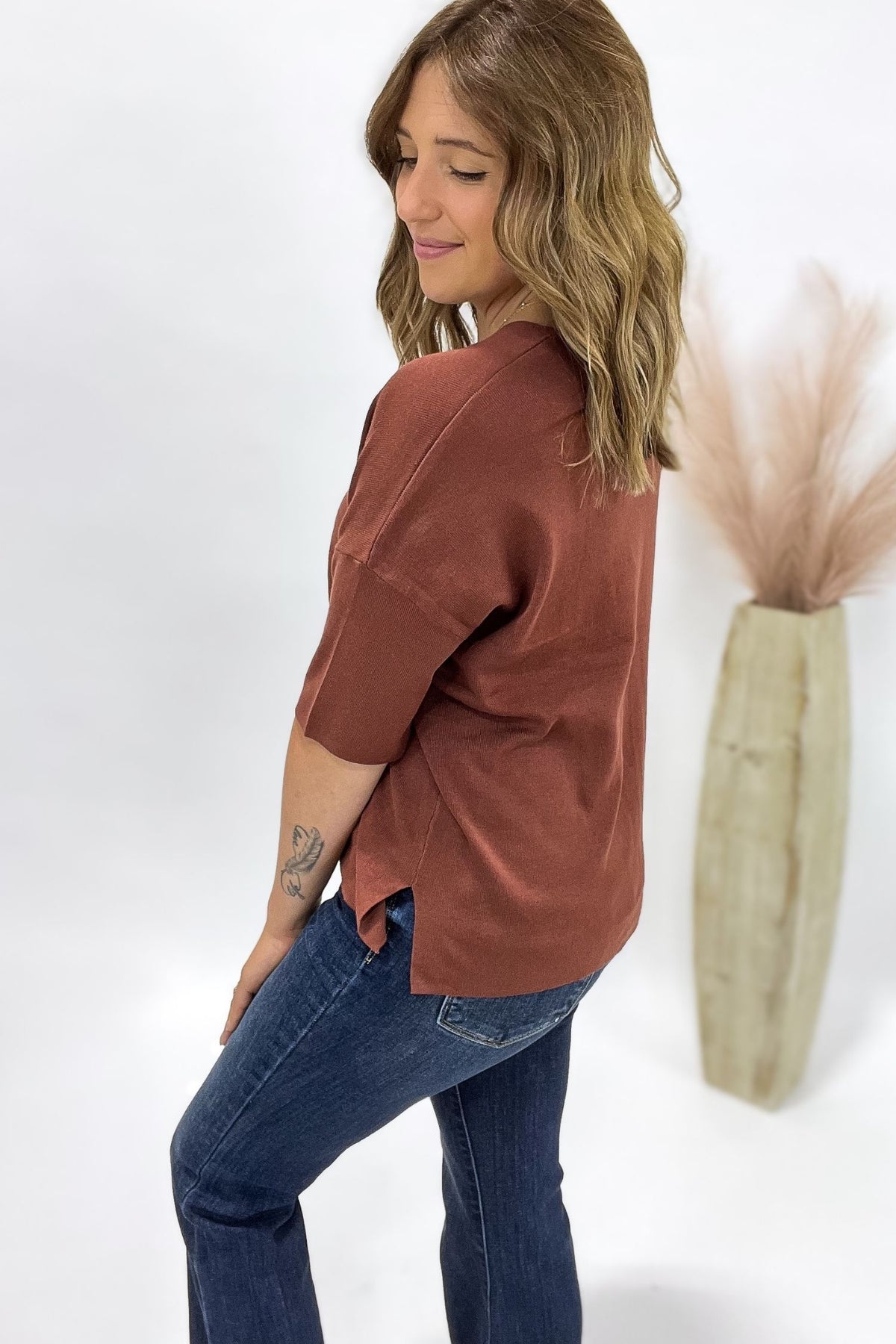 Woman wearing a rust oversized shirt and blue jeans against a white background