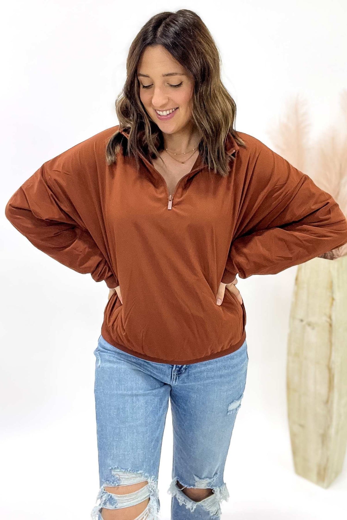 Woman wearing a copper pullover with a zipper and blue jeans on a white background
