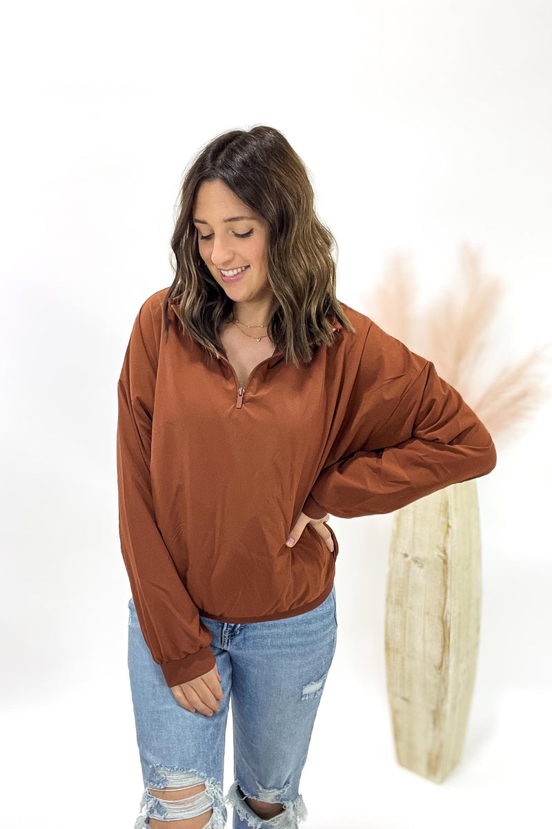 Woman wearing a copper long-sleeve top and blue jeans against a white background