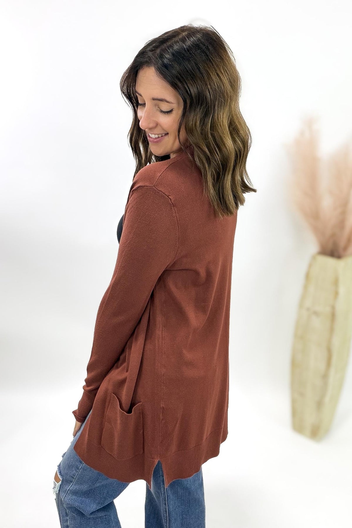 Woman wearing a copper cardigan and blue jeans on a white background