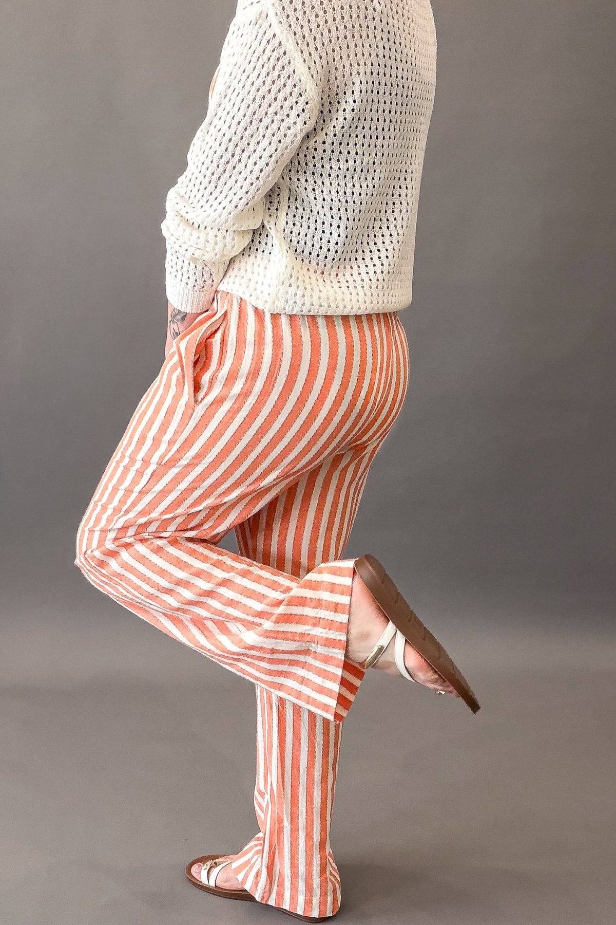 Person wearing a white textured sweater and coral and white striped pants on a gray background