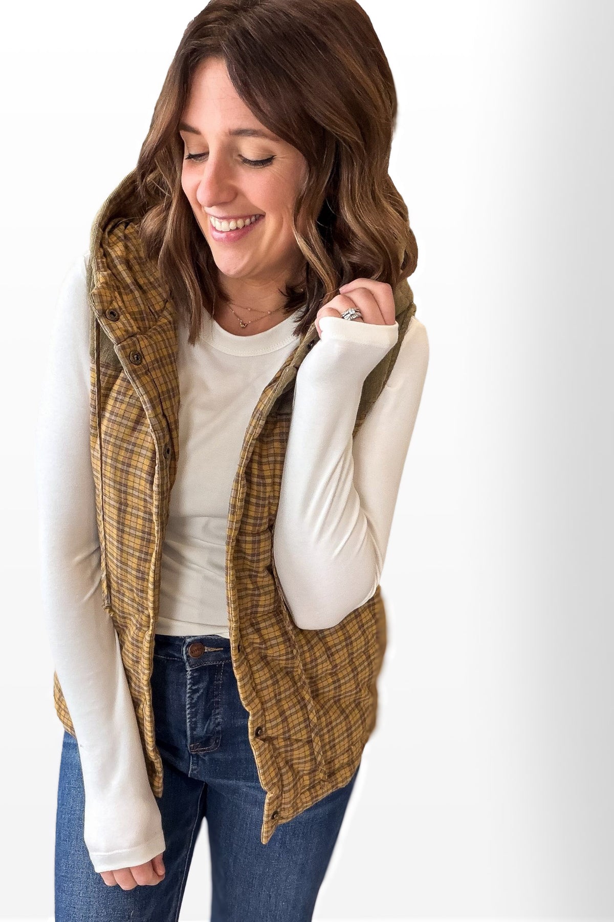 Woman wearing a plaid vest over a white long-sleeve shirt on a white background