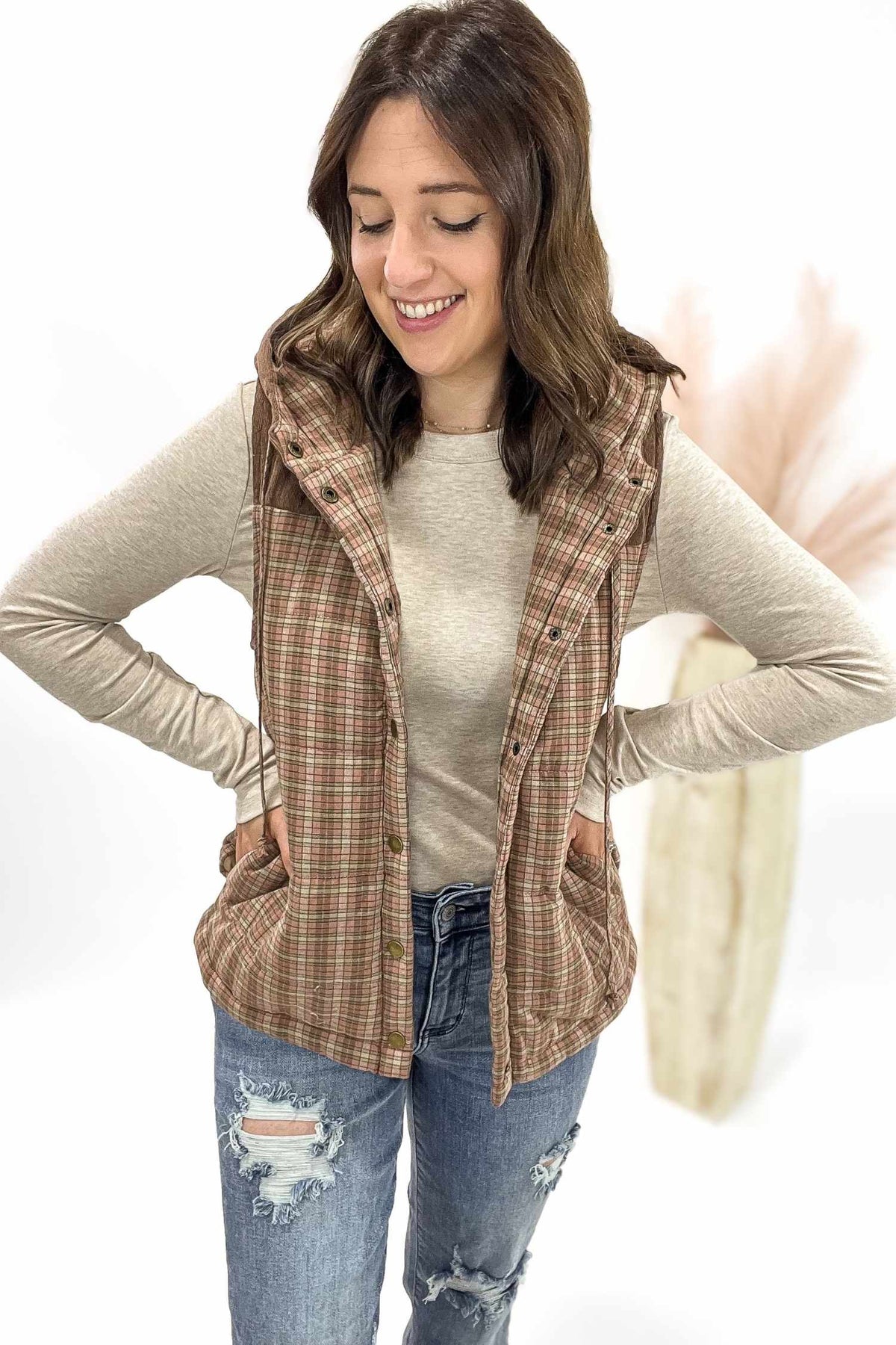 Woman wearing a plaid vest over a beige long-sleeve shirt and jeans on a white background