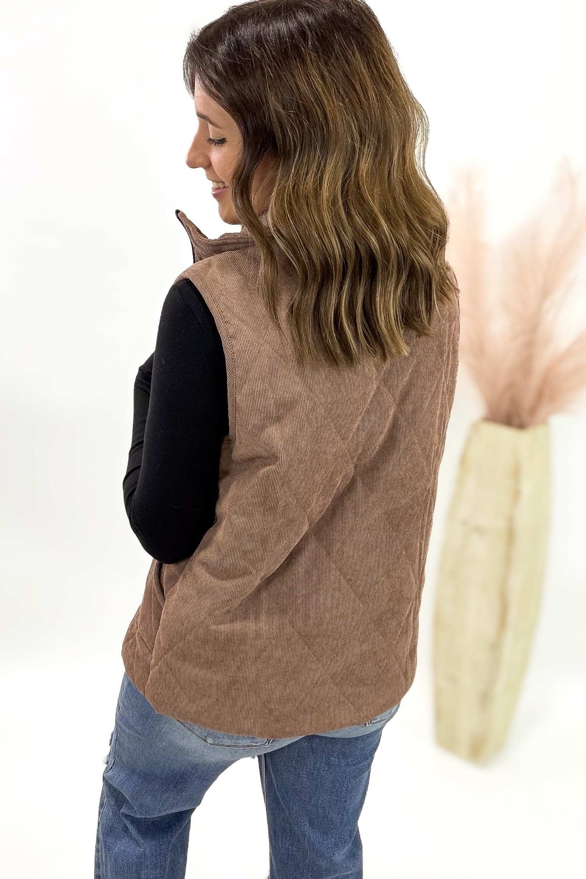 Woman wearing a brown vest over a black shirt and blue jeans on a white background