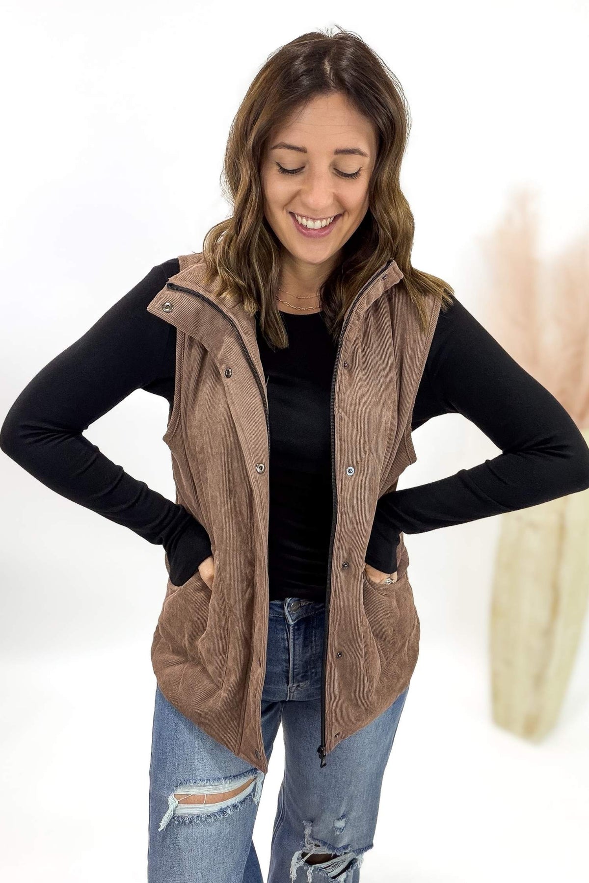 Woman wearing a brown vest over a black long-sleeve shirt with a white background