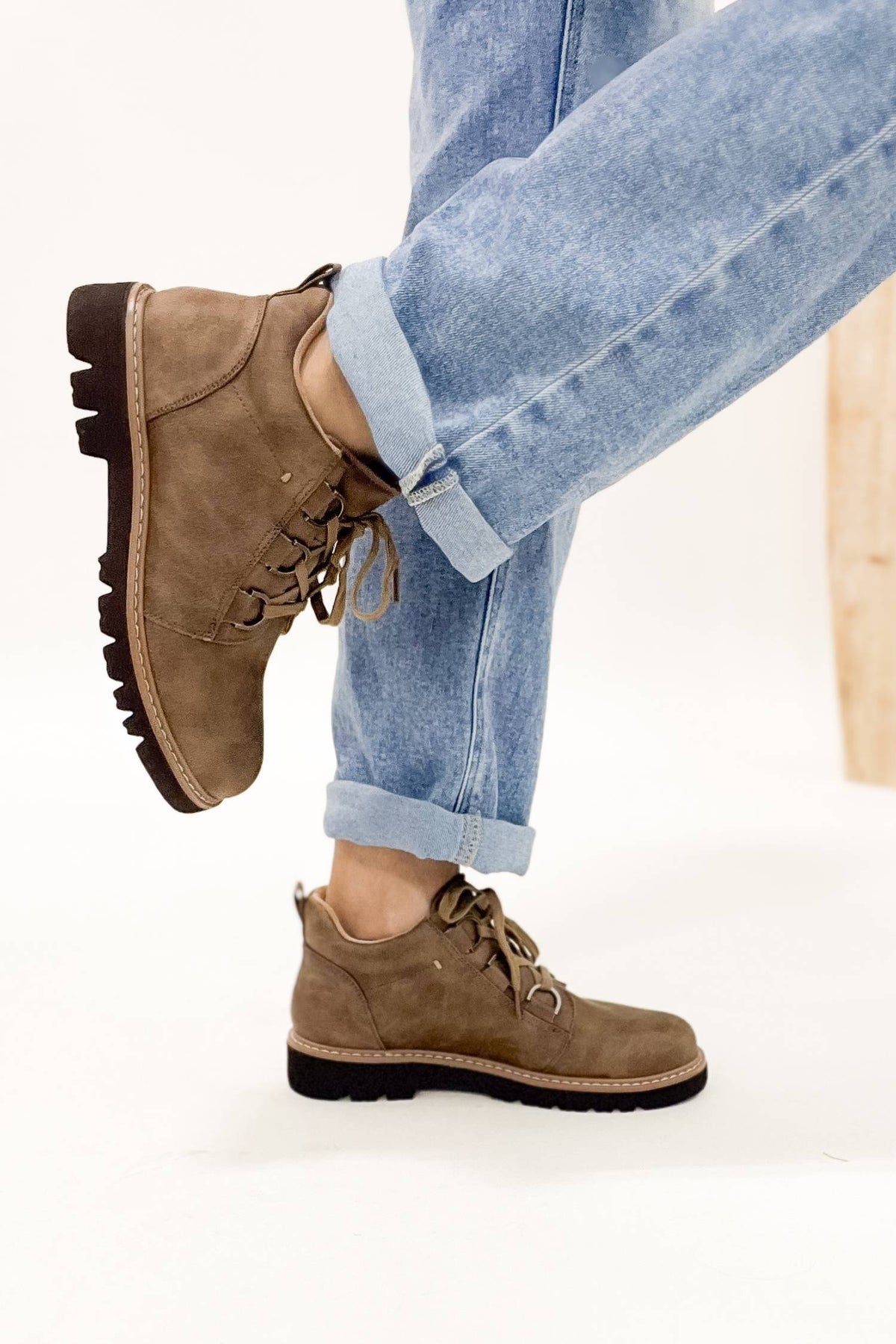 Brown suede boots worn with rolled-up blue jeans on a white background