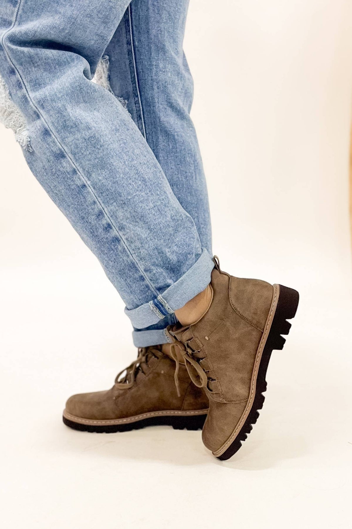 Brown suede boots worn with light blue jeans on a white background