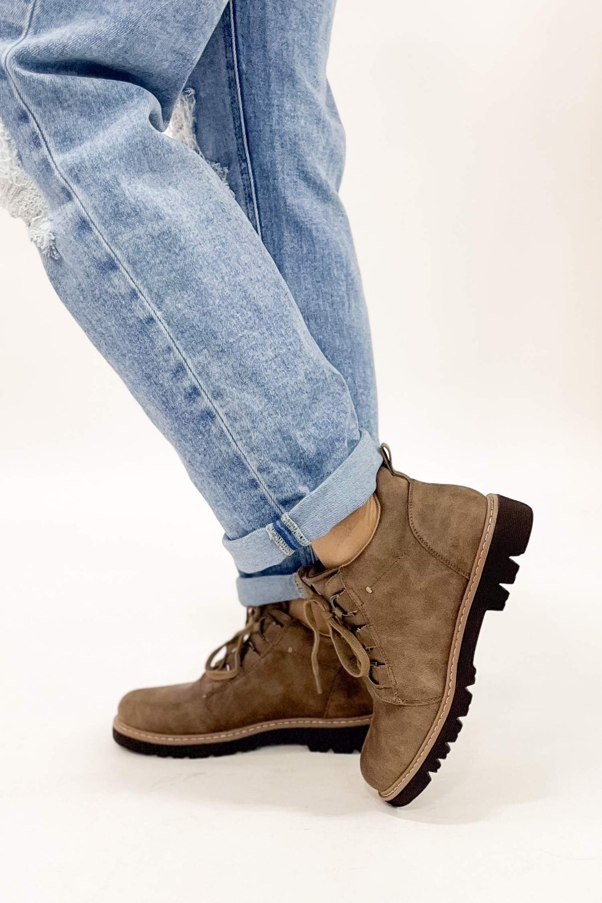 Brown suede boots worn with light blue jeans on a white background