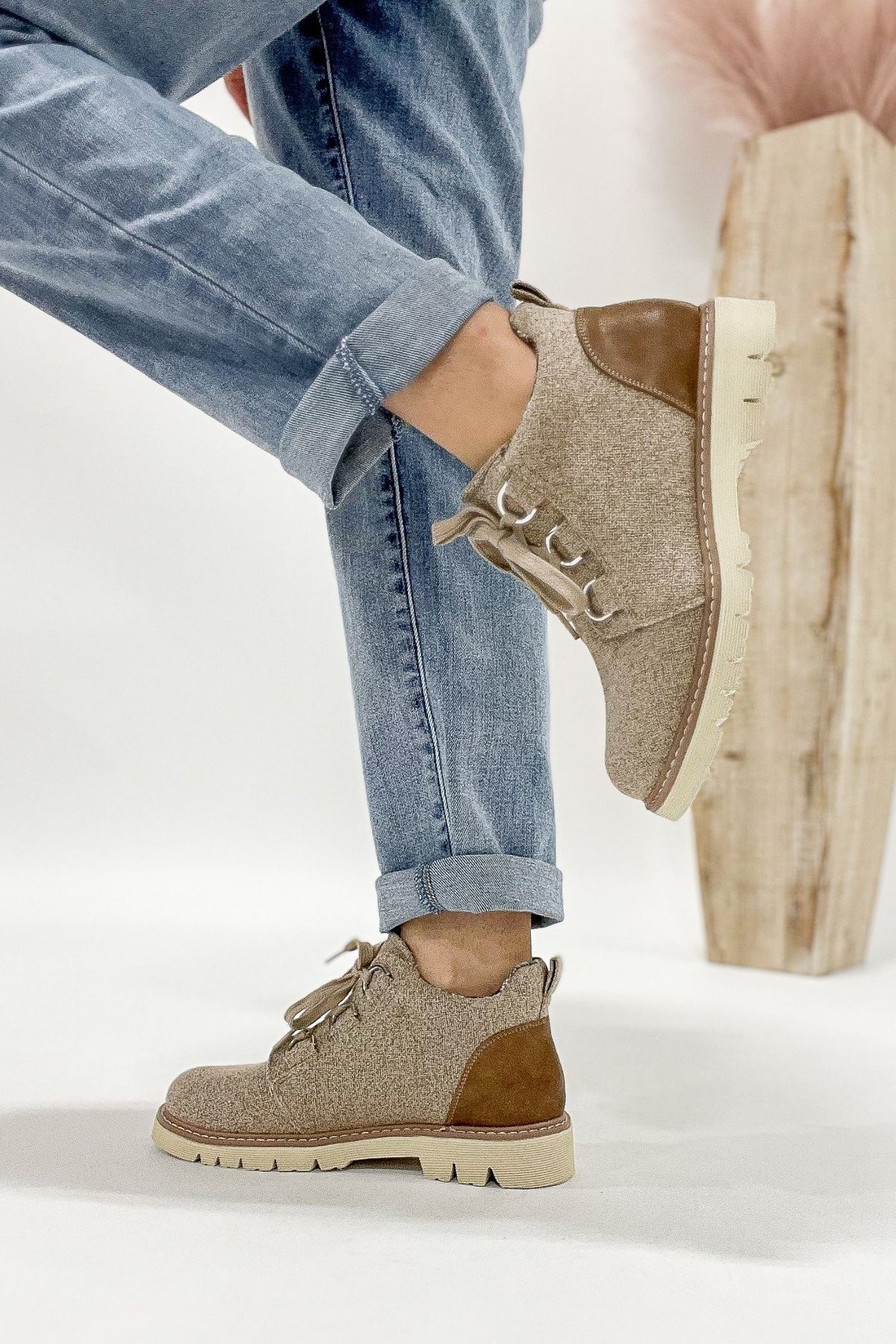 Person wearing brown and beige boots with rolled-up jeans on a white background