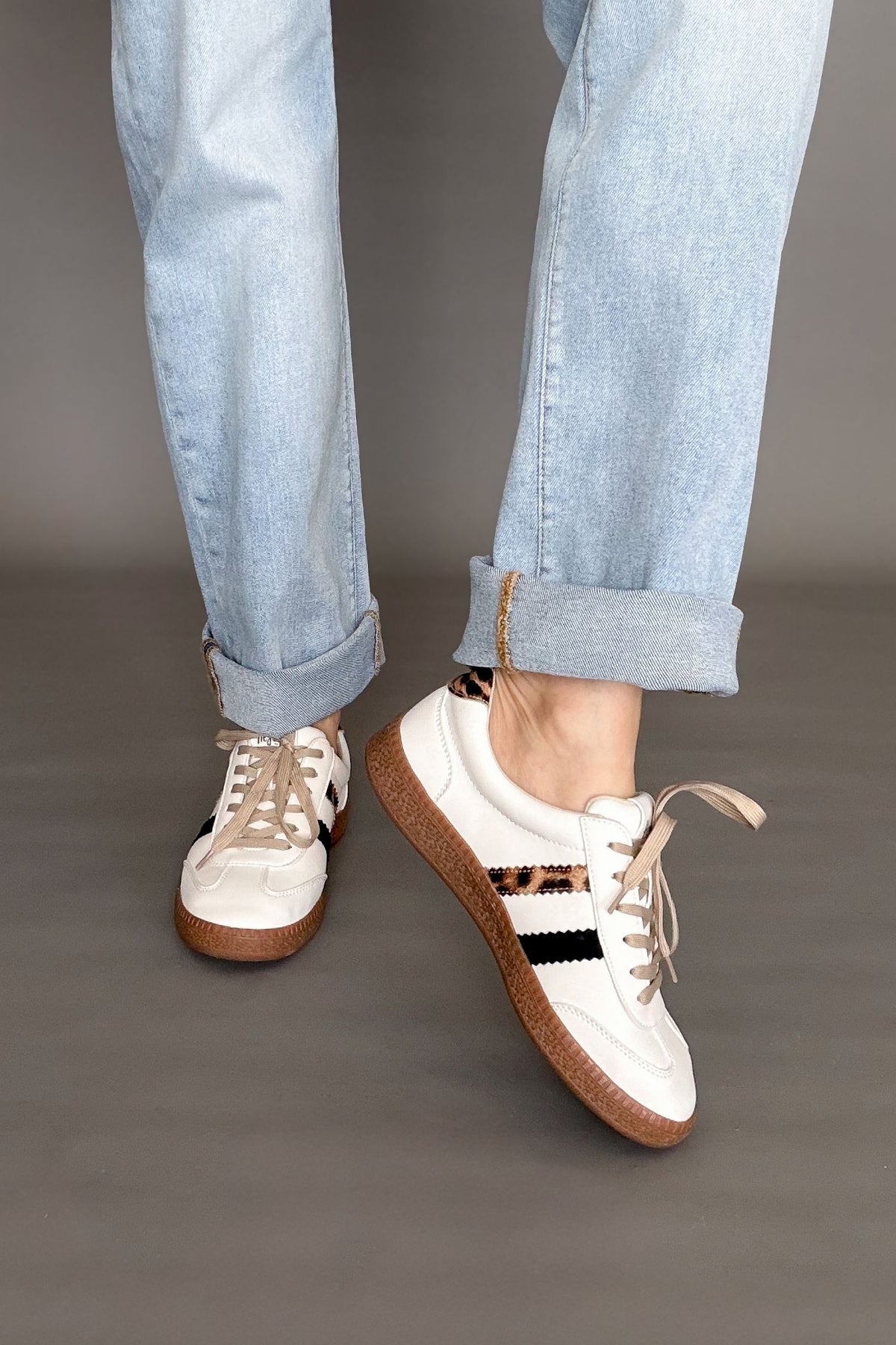 Corkys White sneakers with brown soles worn with light blue jeans on a gray background