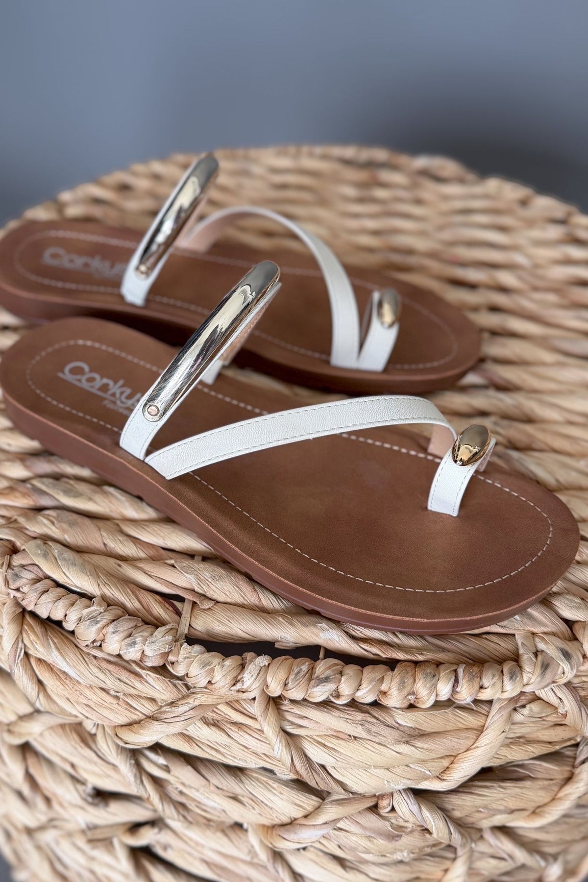 Brown and white sandals with gold accents on a woven surface