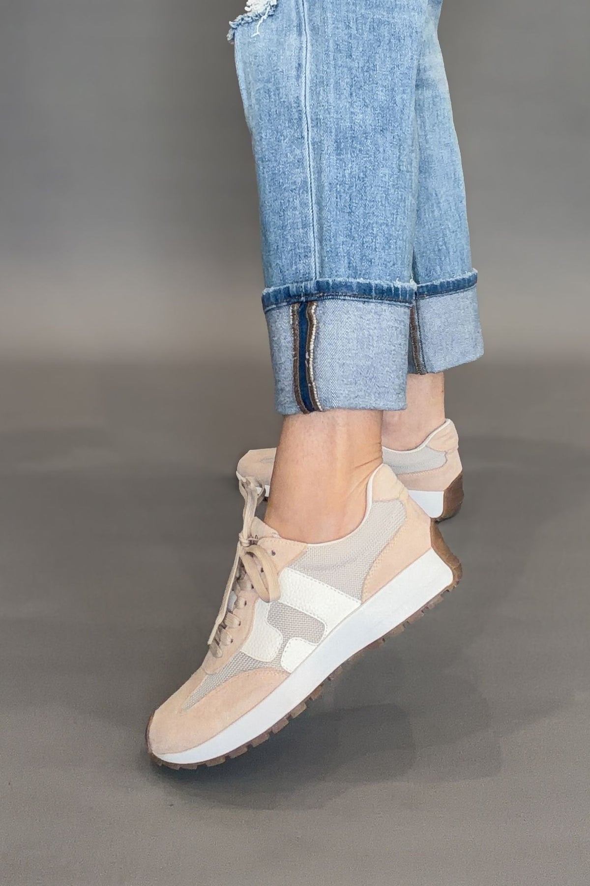 Corkys Beige and white sneakers worn with light blue jeans on a gray background