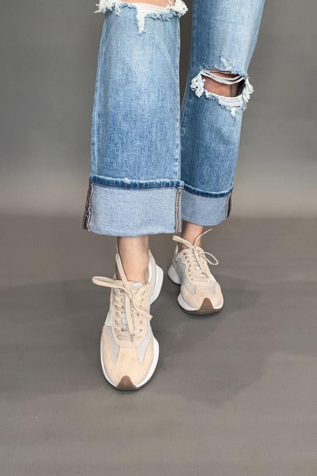 Corkys beige sneakers on a plain background worn with light blue jeans