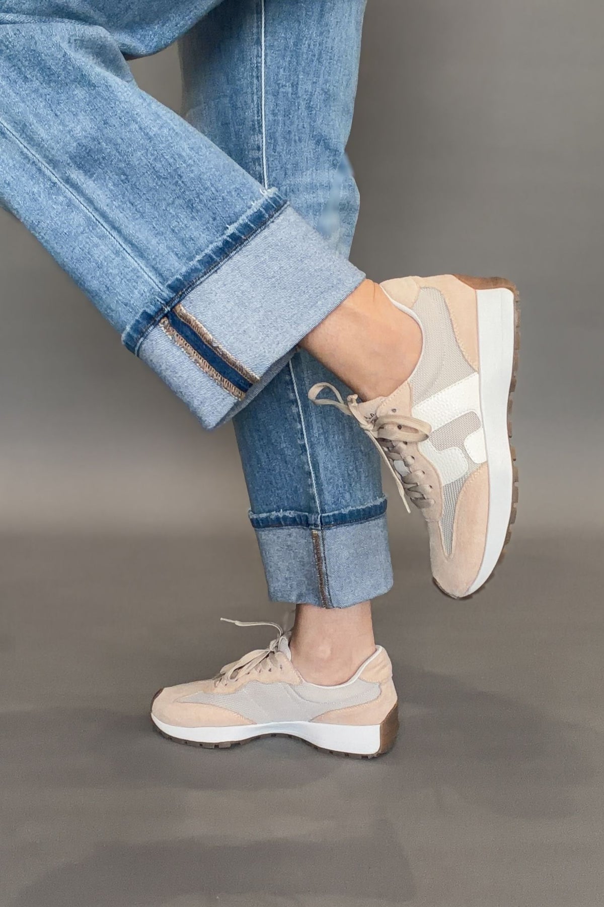 Corkys Beige sneakers worn with rolled-up blue jeans on a gray background