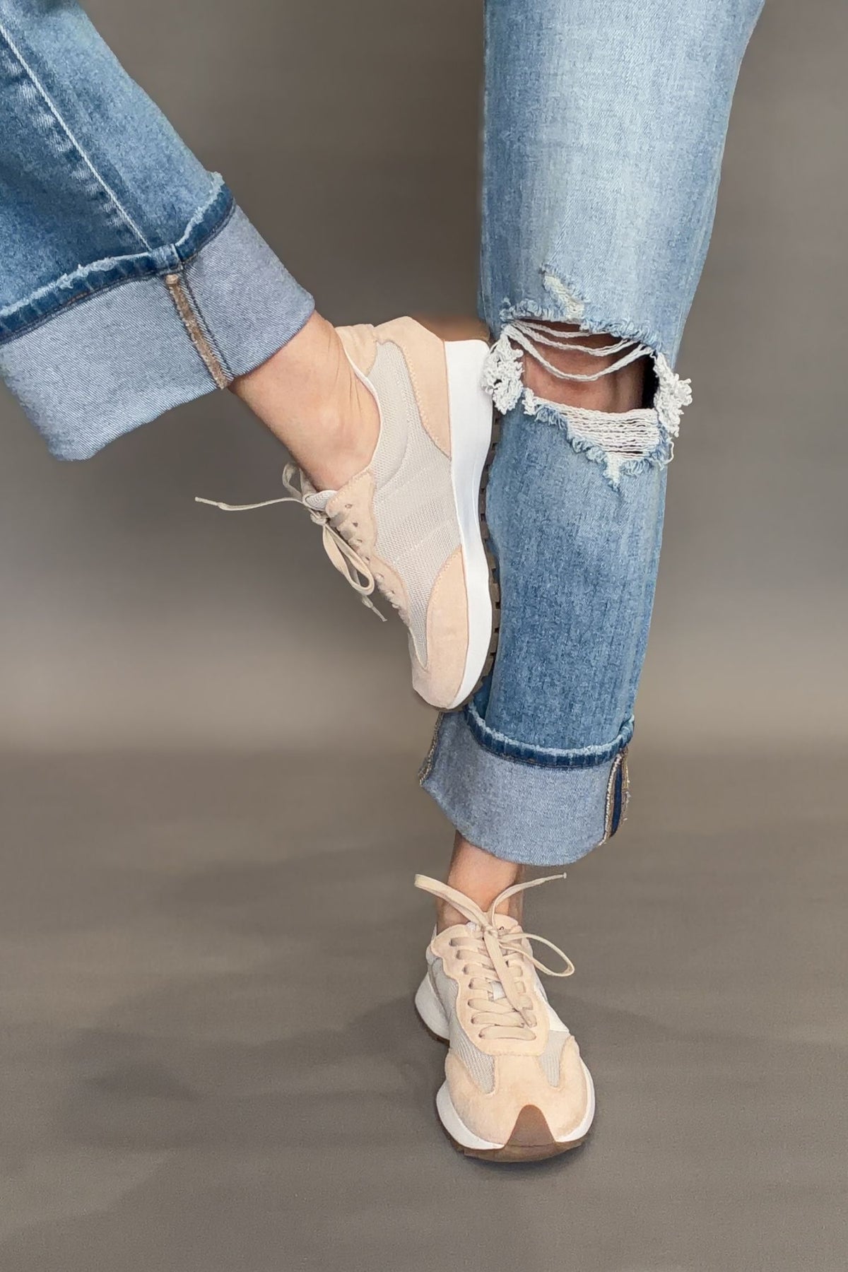 Corkys Beige sneakers worn with ripped blue jeans on a gray background